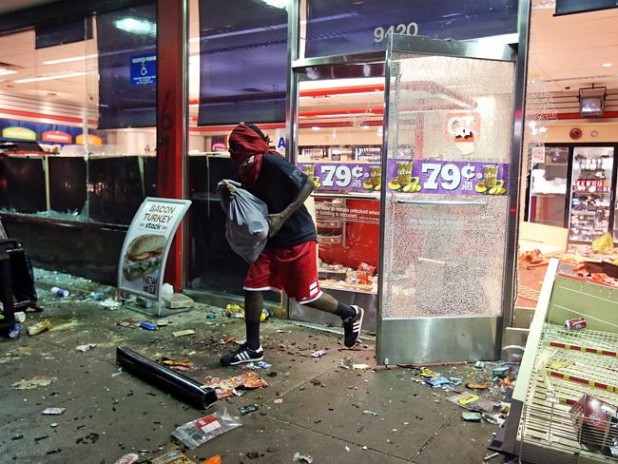 A man leaves a store on Sunday, Aug. 10, 2014, in Ferguson, Mo. A few thousand people crammed a suburban St. Louis street Sunday night at a vigil for unarmed 18-year-old Michael Brown shot and killed by a police officer, while afterward several car windows were smashed and stores were looted as people carried away armloads of goods as witnessed by an an Associated Press reporter. (AP Photo/St. Louis Post-Dispatch, David Carson)
