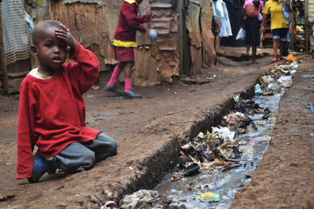 A_young_boy_sits_over_an_open_sewer_in_the_Kibera_slum_Nairobi